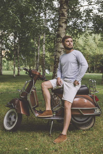 fashionable young man with beard riding a retro scooter in the street - Фото, зображення