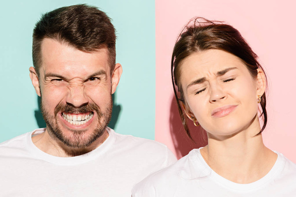 Closeup portrait of young couple, man, woman. One being excited happy smiling, other serious, concerned, unhappy on pink and blue background. Emotion contrasts - Фото, изображение