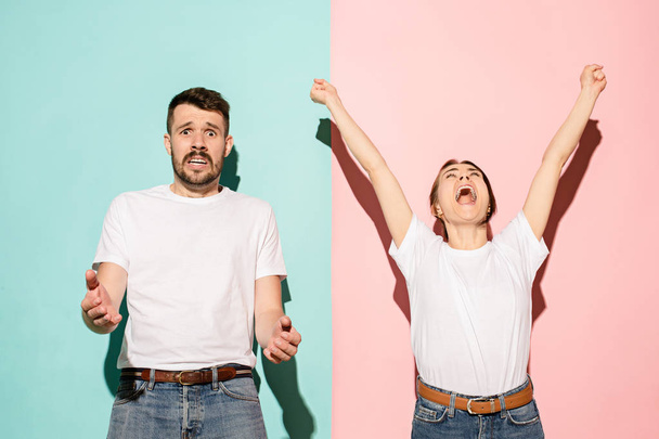 Closeup portrait of young couple, man, woman. One being excited happy smiling, other serious, concerned, unhappy on pink and blue background. Emotion contrasts - Photo, image