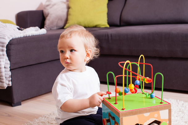 Infant baby boy playing indoors with toy sitting on soft carpet - Foto, Imagen