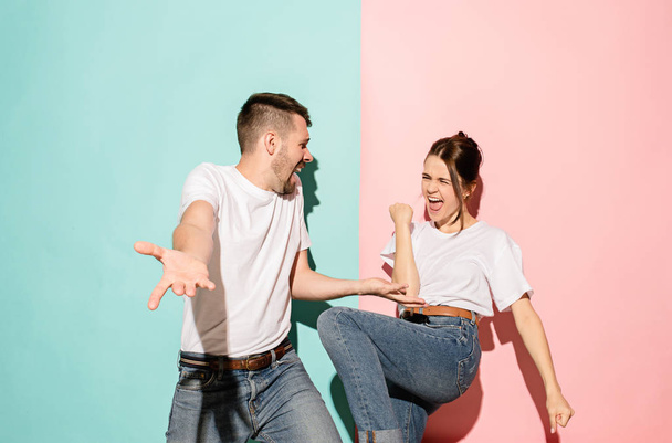 Closeup portrait of young couple, man, woman. One being excited happy smiling, other serious, concerned, unhappy on pink and blue background. Emotion contrasts - Zdjęcie, obraz