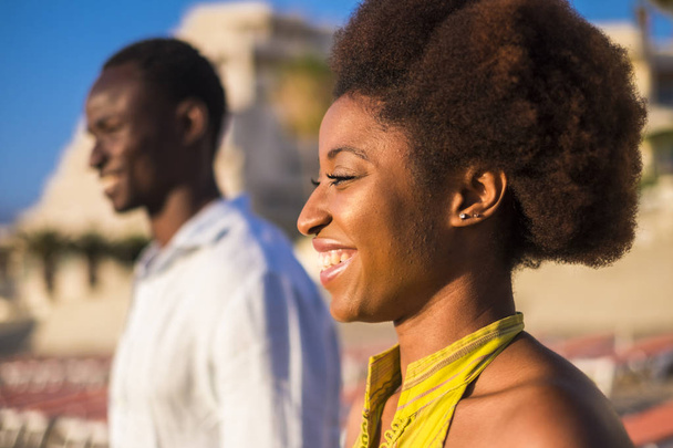 güzel siyah ırk Afrikalı model güneşe gülümseyen güzel gülümsüyor portresi. başka bir siyah adam arka plan üzerinde defocused. dostluk ve sevgi ile birlikte yaz tatilinde gör - Fotoğraf, Görsel