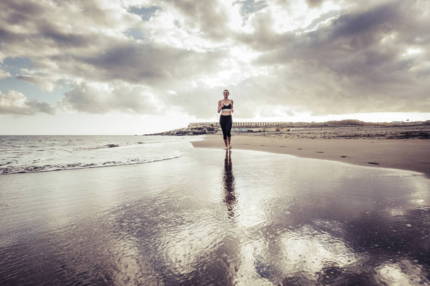 samotny runner Pani Młoda kaukaski dziewczyna na plaży w stylu boso uruchomiony na brzegu. fale i ocean sport pojęcia działalności. niesamowity zachód słońca i dzień. uruchomić na wybrzeżu. - Zdjęcie, obraz