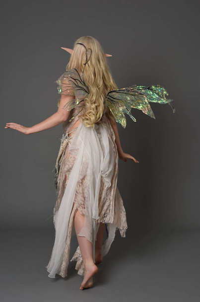 full length portrait of blonder wearing fairy costume, standing pose with back to the camera.  grey studio background. - Photo, Image