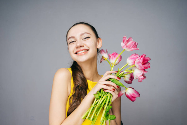 a laughing young girl in a yellow dress is holding a bouquet of fragrant pink flowers, a good mood - Photo, Image