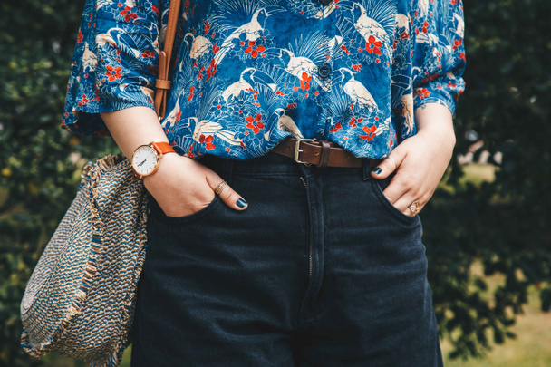 street style fashion details. close up, fashion blogger wearing a summer shirt and a white and brown analog wrist watch, holding a beautiful round straw purse. perfect summer fashion accessories. - Photo, Image