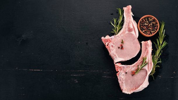Raw steak on the bone with spices and vegetables. On a wooden background. Top view. Copy space. - Foto, imagen