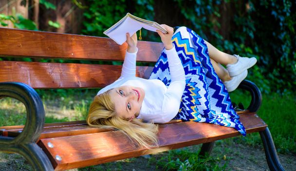 Interesting book. Smart and pretty. Smart lady relaxing. Girl lay bench park relaxing with book, green nature background. Woman spend leisure with book. Girl reading outdoors while relaxing on bench - Photo, Image