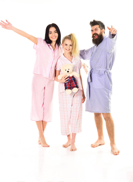 Man with beard and mustache, cute blonde and brunette girls with toy bear full of energy. Girls with bearded macho in pajamas and robe in morning, isolated white background. Good mood concept - Photo, Image