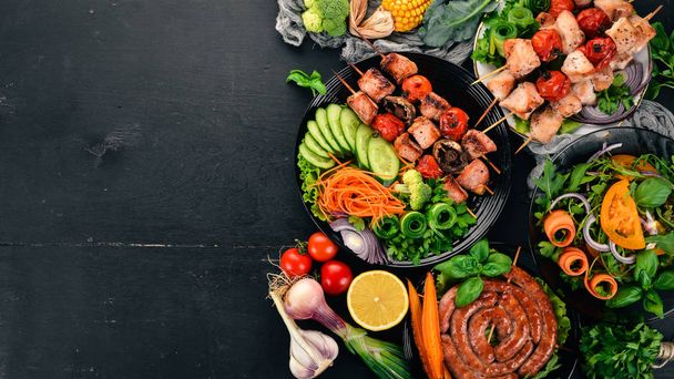 Assortment of baked barbecue meat. Sausages, skewers, fresh vegetables. Tomatoes, onions, garlic. On a wooden background. Copy space. - Photo, image