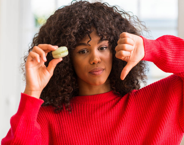 Afrikai-amerikai nő gazdaság macaron dühös arccal, negatív előjellel mutatja nem szeretik a hüvelykujját lefelé, elutasítás koncepció - Fotó, kép