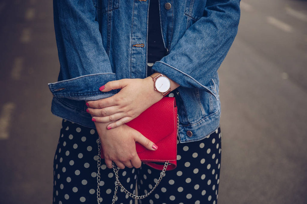 κομψή γυναίκα στο σακάκι τζιν κρατώντας ένα κόκκινο πορτοφόλι και φοράει ένα ροζ χρυσό καρπό ρολόι. Μόδα στυλ του δρόμου - Φωτογραφία, εικόνα