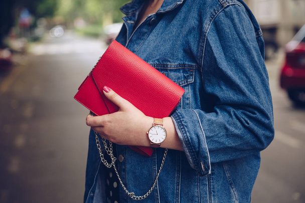 Stylische Frau in Jeansjacke mit roter Handtasche und roségoldener Armbanduhr. Street-Style-Mode - Foto, Bild
