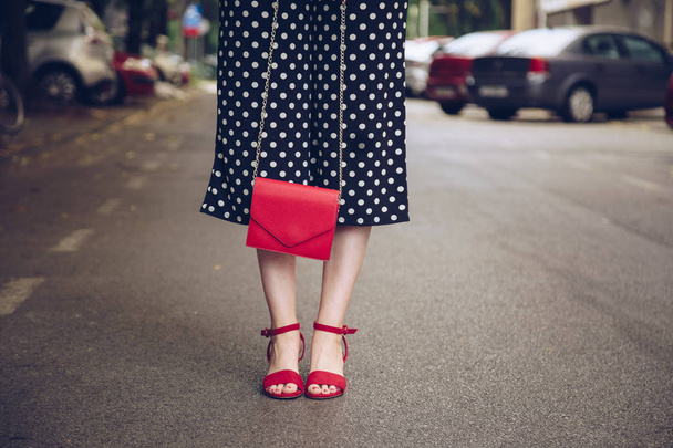 stylish woman in polka dot culottes and red high heel shoes holding a red purse and crossing the road.  street style fashion - Valokuva, kuva