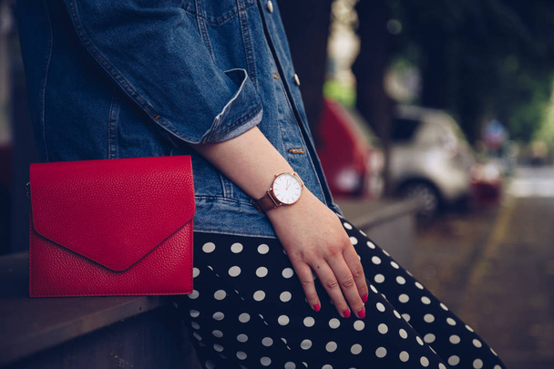 стильна жінка в джинсовій куртці тримає червоний гаманець і носить золотий наручний годинник троянди. мода вуличного стилю
 - Фото, зображення