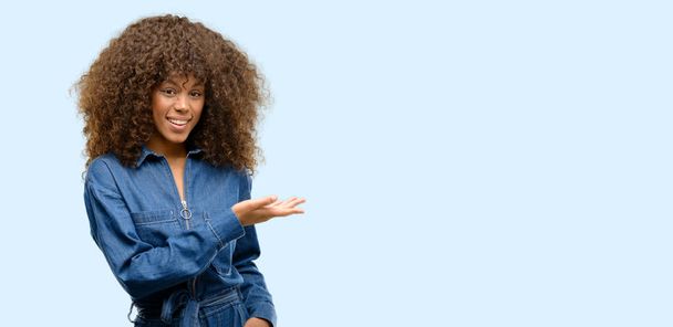 African american woman wearing blue jumpsuit holding something in empty hand - Photo, Image