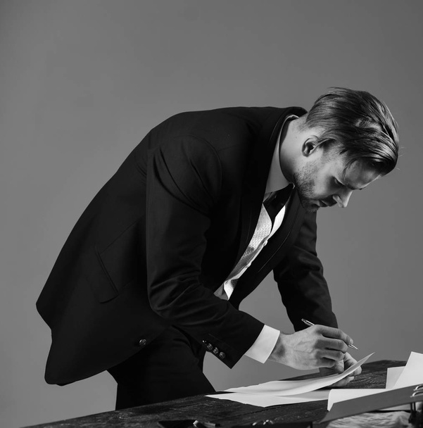 Businessman signs contract by pen on dark background. Signing documents concept. Man with serious face writes on docum - Φωτογραφία, εικόνα