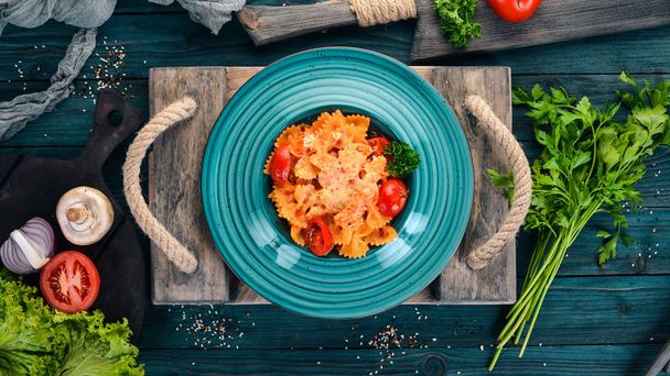 Farfalle pasta with tomatoes and parmesan cheese. Italian cuisine. On a wooden background. Top view. Copy space. - Photo, image