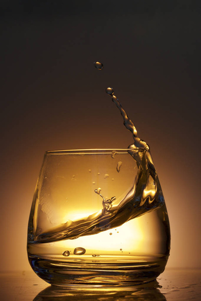 Splash the liquid in a glass. Photographed on a colored background. Backlight control. - Foto, Imagen