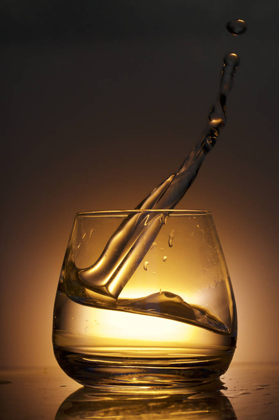 Splash the liquid in a glass. Photographed on a colored background. Backlight control. - Fotografie, Obrázek