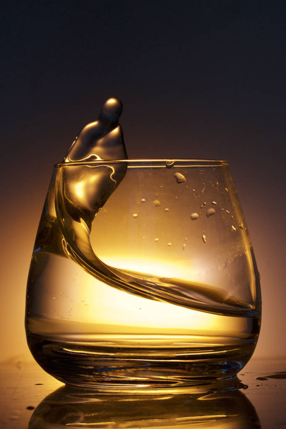 Splash the liquid in a glass. Photographed on a colored background. Backlight control. - 写真・画像