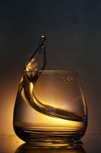 Splash the liquid in a glass. Photographed on a colored background. Backlight control. - Φωτογραφία, εικόνα