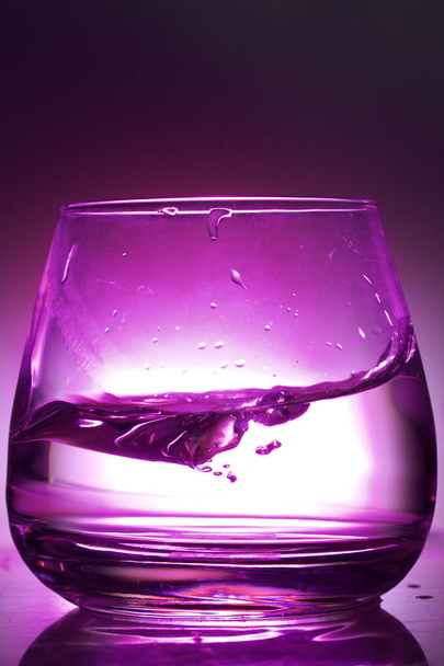 Splash the liquid in a glass. Photographed on a colored background. Backlight control. - Foto, immagini