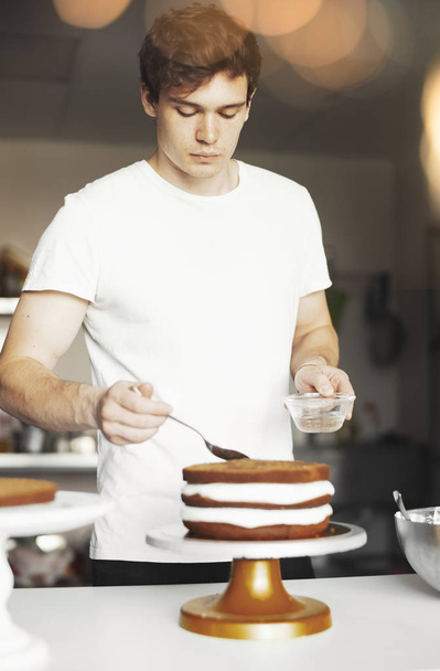 Young attractive man smearing sugar syrup on chocolate cake. - Foto, Imagen