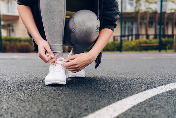 slim girl tie lacets sur ses chaussures de course, sur le terrain de sport en plein air
 - Photo, image