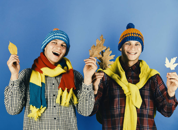 Twin brothers wearing warm hats and scarves hold dry leaves Siblings enjoy autumn time. Autumn weather and twins life concept - Foto, afbeelding
