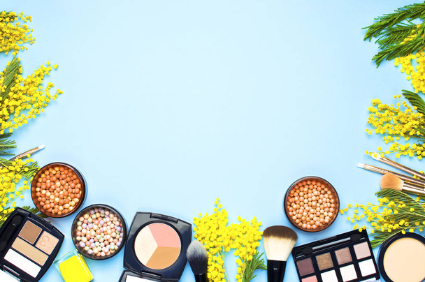 Zestaw kosmetyków dekoracyjnych pędzle do makijażu proszku Rouge Eyeshadow korektor i kwiatów mimozy na niebieskim tle. Widok z góry Akcesoria do makijażu - Zdjęcie, obraz