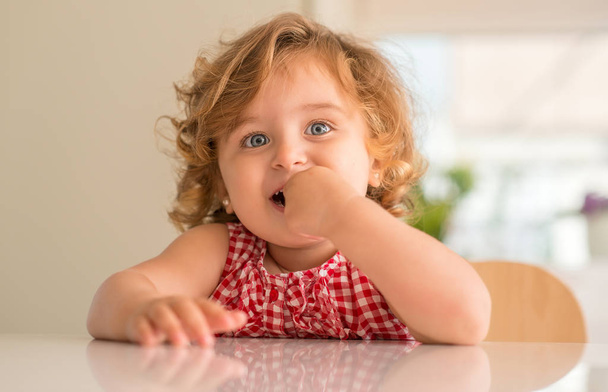 Beautiful blonde child with blue eyes smiling and eating candy at home. - Foto, afbeelding