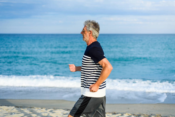 Älterer Mann läuft am Strand, aktiver Lebensstil im Urlaub - Foto, Bild