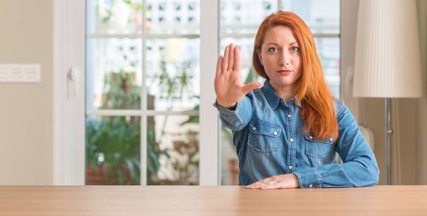 Femme rousse à la maison faisant arrêter de chanter avec la paume de la main. Expression d'avertissement avec geste négatif et sérieux sur le visage
. - Photo, image
