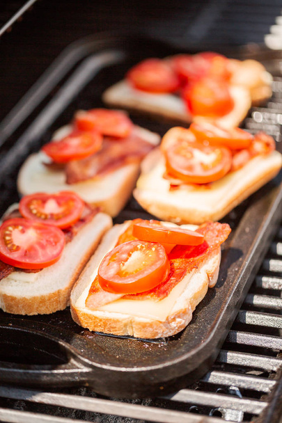 Сэндвич с жареным сыром на гриле с беконом и помидорами на открытом газовом гриле
. - Фото, изображение