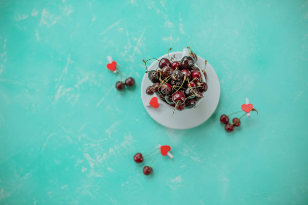 パステル グリーンの背景に分離された白いカップに赤サクランボ赤いハートと甘い果実。夏の組成物、コピー スペース。新鮮な果実と健康菜食生活に美味しい料理 - 写真・画像
