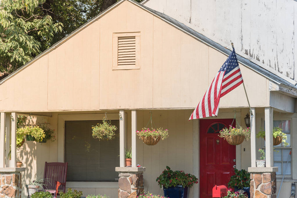 Front porch of typical one story house proudly displaying American flag. Beautiful hanging flower pots - Photo, image
