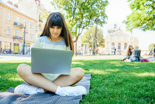 jovem mulher adulta que estabelece com laptop no parque da cidade na grama verde
 - Foto, Imagem