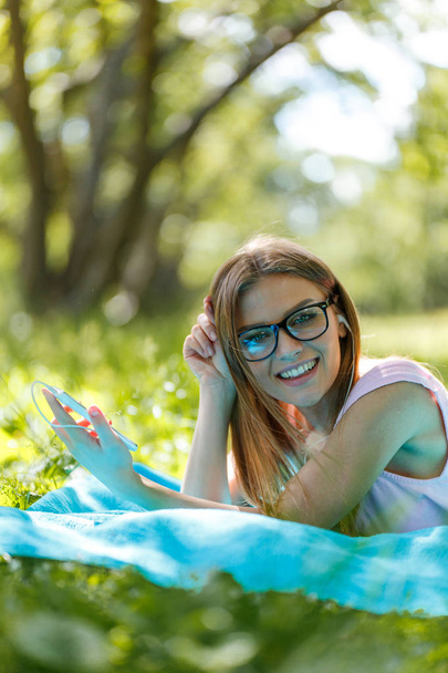 Girl lay down or relaxing on green grass listening music with smartphone in summer or spring - Fotografie, Obrázek