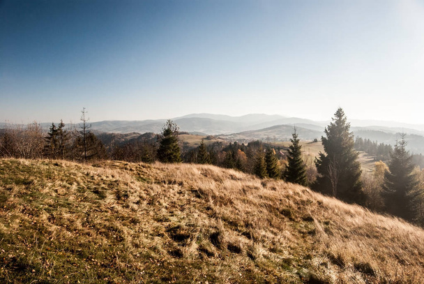 Осенний горный ландшафт с холмами, лугами, деревьями и чистым небом - вид с холма Коцы Замек над деревней Коняков в Бескидских горах Сласки в Польше
 - Фото, изображение