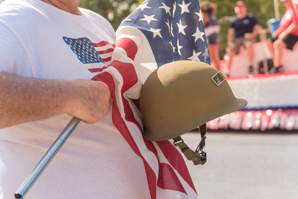Boční pohled bílý veterán hrdě drží vojenské Wwi přilba (helma M1) a USA vlajka. 4. července nebo plakát den veteránů druhé světové války, moderní války. Americký voják vojsk během průvodu lidí sleduje - Fotografie, Obrázek