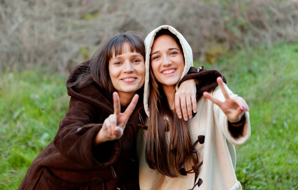 Outdoor portrait of two happy sisters showing peace gesture in a park - Photo, Image