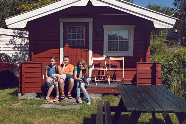 famille heureuse - parents souriants et leurs deux filles assis près de la maison norvégienne rouge traditionnelle, Norwa
 - Photo, image