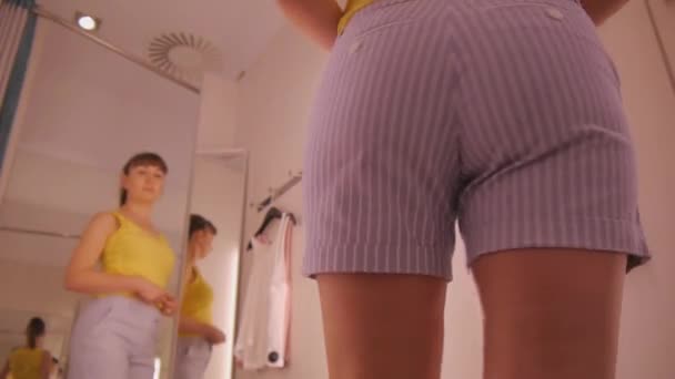 Jonge vrouw proberen op kleding. Lage hoekmening van aantrekkelijke Kaukasische vrouw in de spiegel kijken proberen op korte broek in kleding slaat paskamer. Close-up van de heupen. - Video