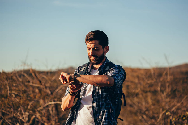 Portrait of a handsome male hiker looking on wrist watch in the desert - Zdjęcie, obraz