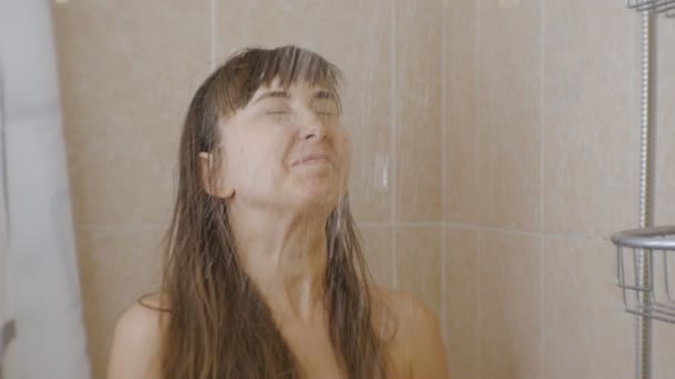 Woman taking a shower. A young smiling caucasian woman looks up while stream of water begins to pour on her face. - Footage, Video