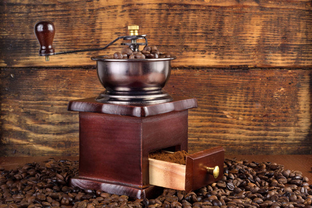 Традиционная деревянная кофейная мельница с жареными кофейными зёрнами и деревянным фоном. Концепция ретро и винтажных продуктов питания и напитков
 - Фото, изображение