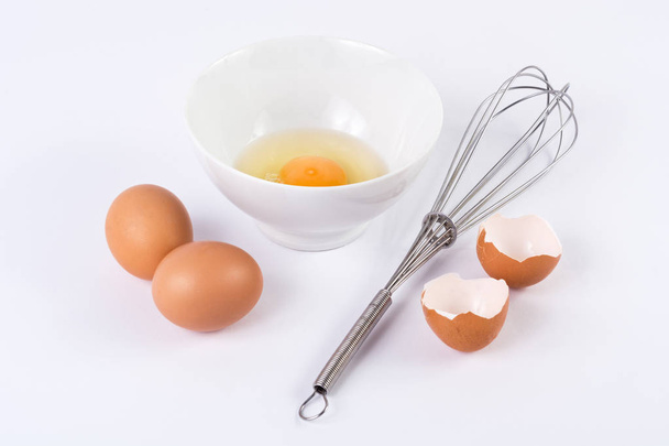 Uovo bianco con il tuorlo in ciotola e altre uova voci con una frusta su sfondo bianco. Concetto di cibo e cucina
 - Foto, immagini