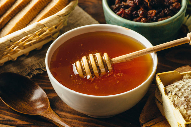Miel dans un bol en céramique blanche, cuillère goutteur de miel, nid d'abeille fait maison sur table en bois rustique
 - Photo, image
