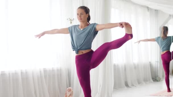 woman doing yoga hand-to-big-toe pose at studio - 映像、動画